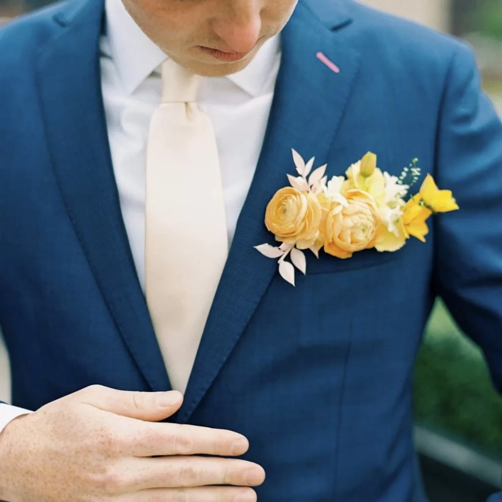 Groom looking down at his pocket boutonniere in his blue jacket.